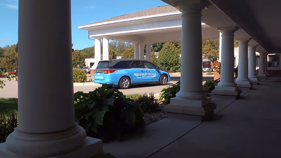 Covered entrance with white columns and a blue Friendship Village van parked outside.