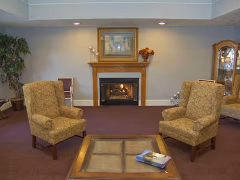 Common sitting area with two upholstered armchairs, a coffee table, and a lit fireplace beneath a framed picture.