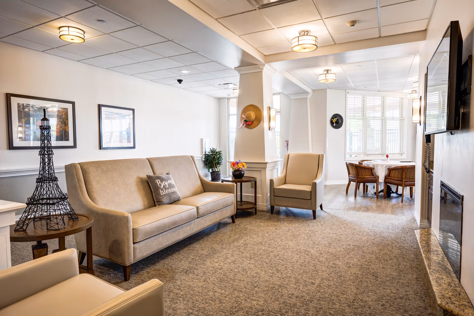 Bright, furnished lounge with a sofa, armchairs, side tables and a small dining nook by bay windows.