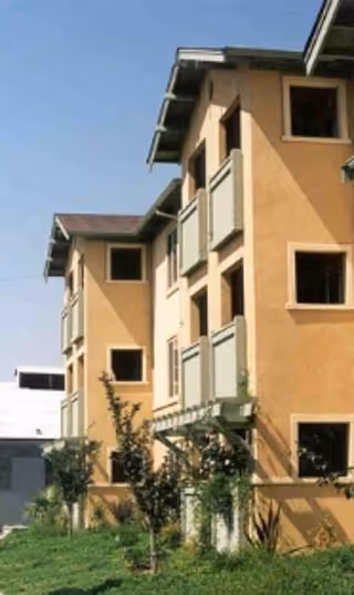 Exterior view of a three-story orange senior living facility with balconies and greenery.