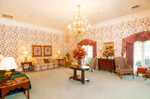 Elegant living room in Magnolia Estates of Oconee with floral wallpaper, chandelier, and seating.