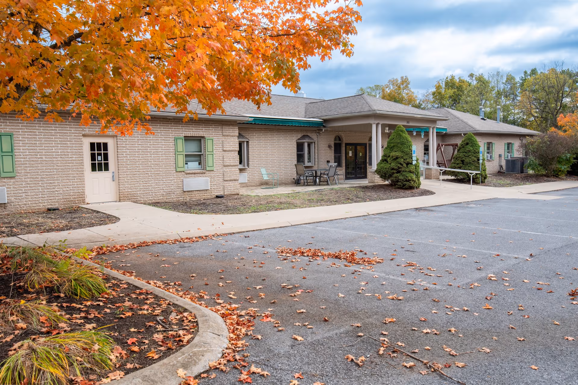 Exterior view of Greenhills Village building with autumn leaves and a pathway.