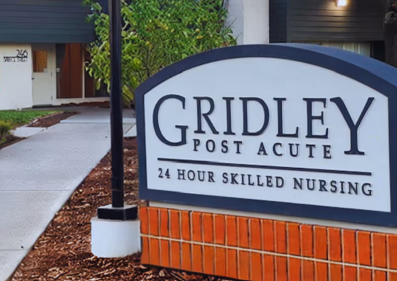 Entrance sign reading "Gridley Post Acute — 24 Hour Skilled Nursing" with the facility building and walkway visible behind it.