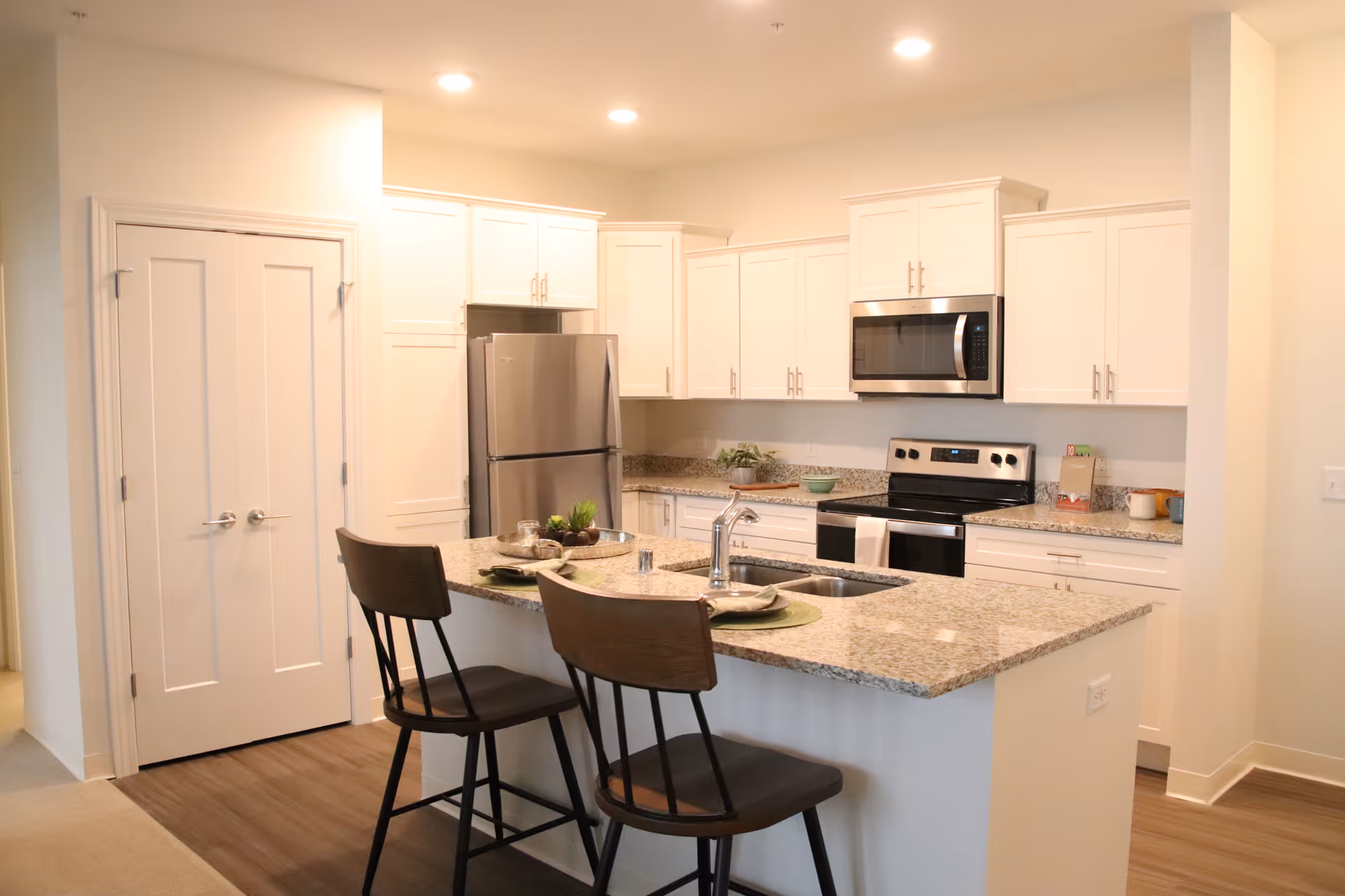 Bright modern kitchen with a granite island, two bar stools, stainless steel appliances, and white cabinets.