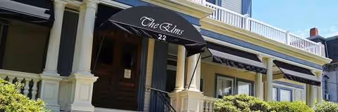 Front entrance of The Elms senior living with columns and a black awning.