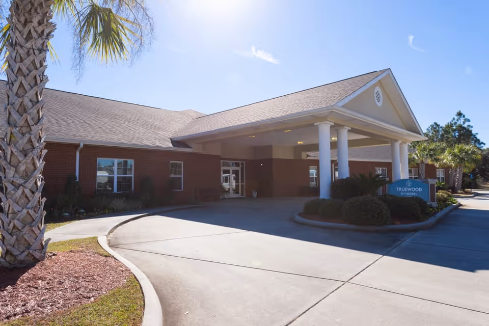 Front entrance of a single-story brick senior living facility with a covered porte-cochere and landscaped driveway.