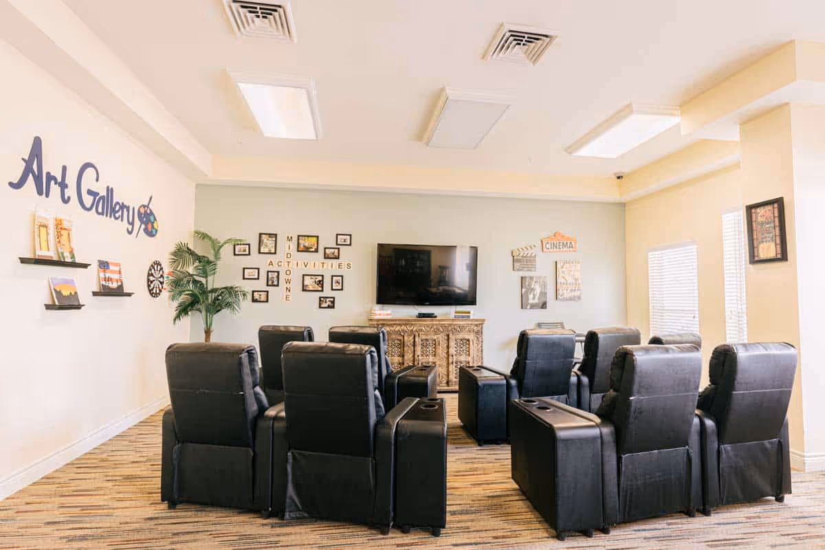 A communal activity/media room with rows of black recliner chairs facing a wall-mounted TV and themed wall decor reading 'Art Gallery' and 'Cinema'.