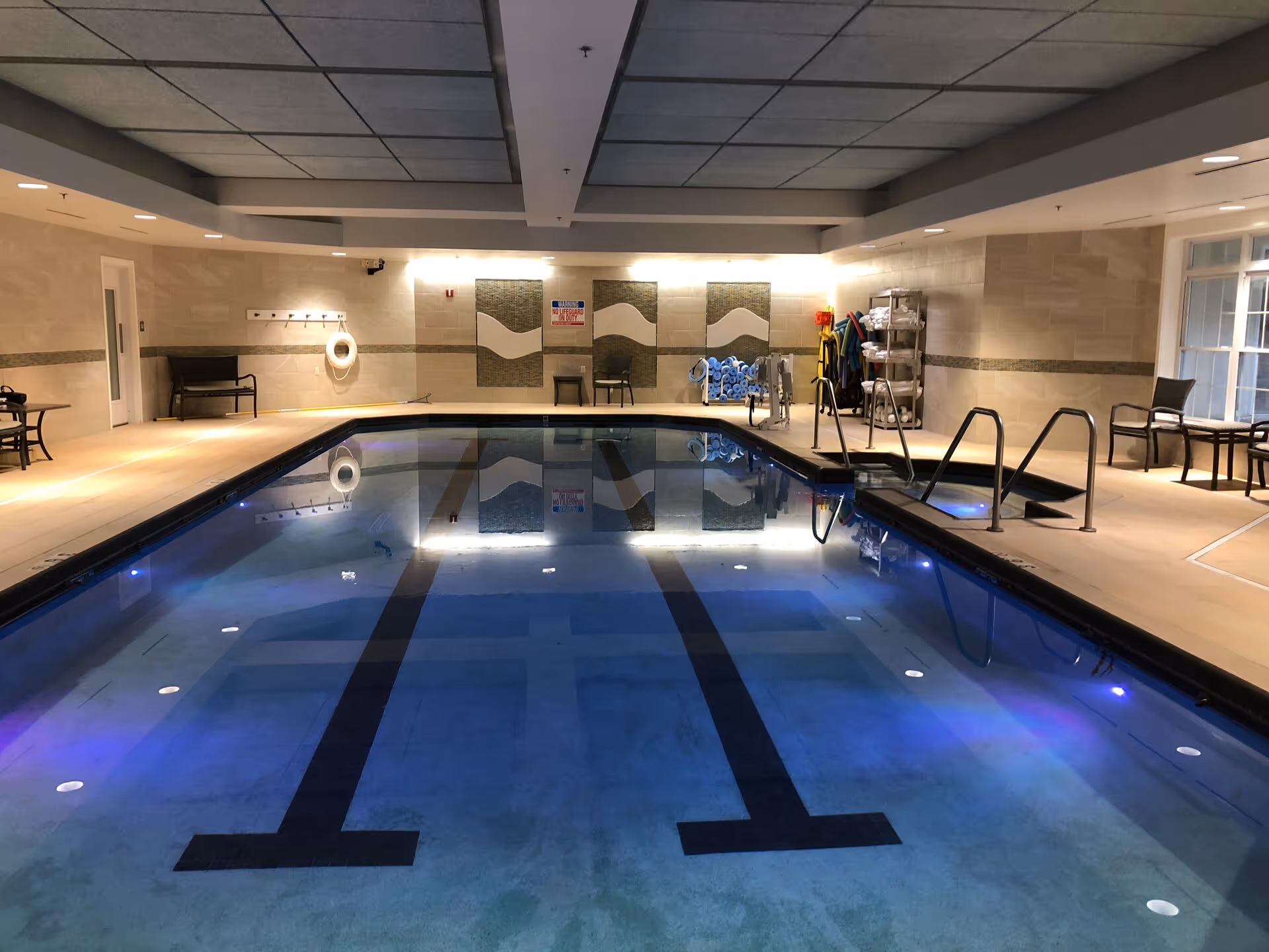 Indoor swimming pool with lane markings, deck chairs, and pool equipment in a well-lit room.