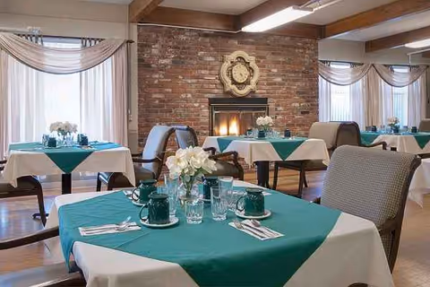 Dining room with green tablecloths, white napkins, floral centerpieces, and a brick fireplace.