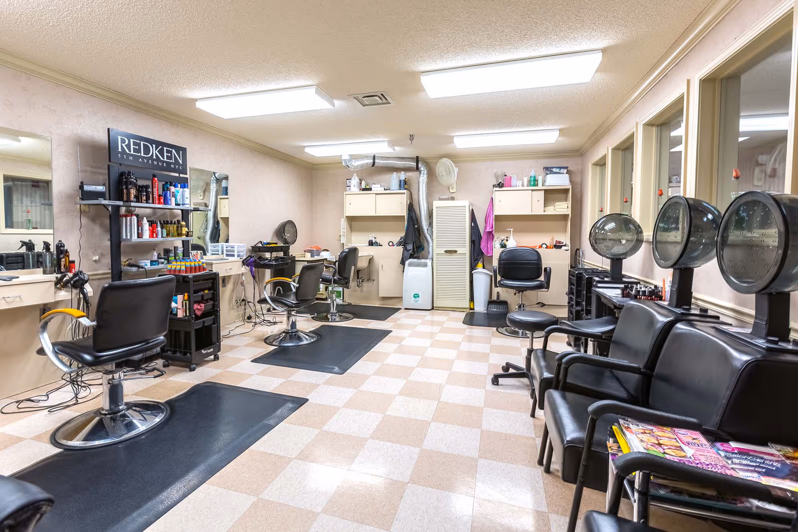 Interior salon room with styling chairs, hooded hair dryers, product shelves, and waiting chairs.