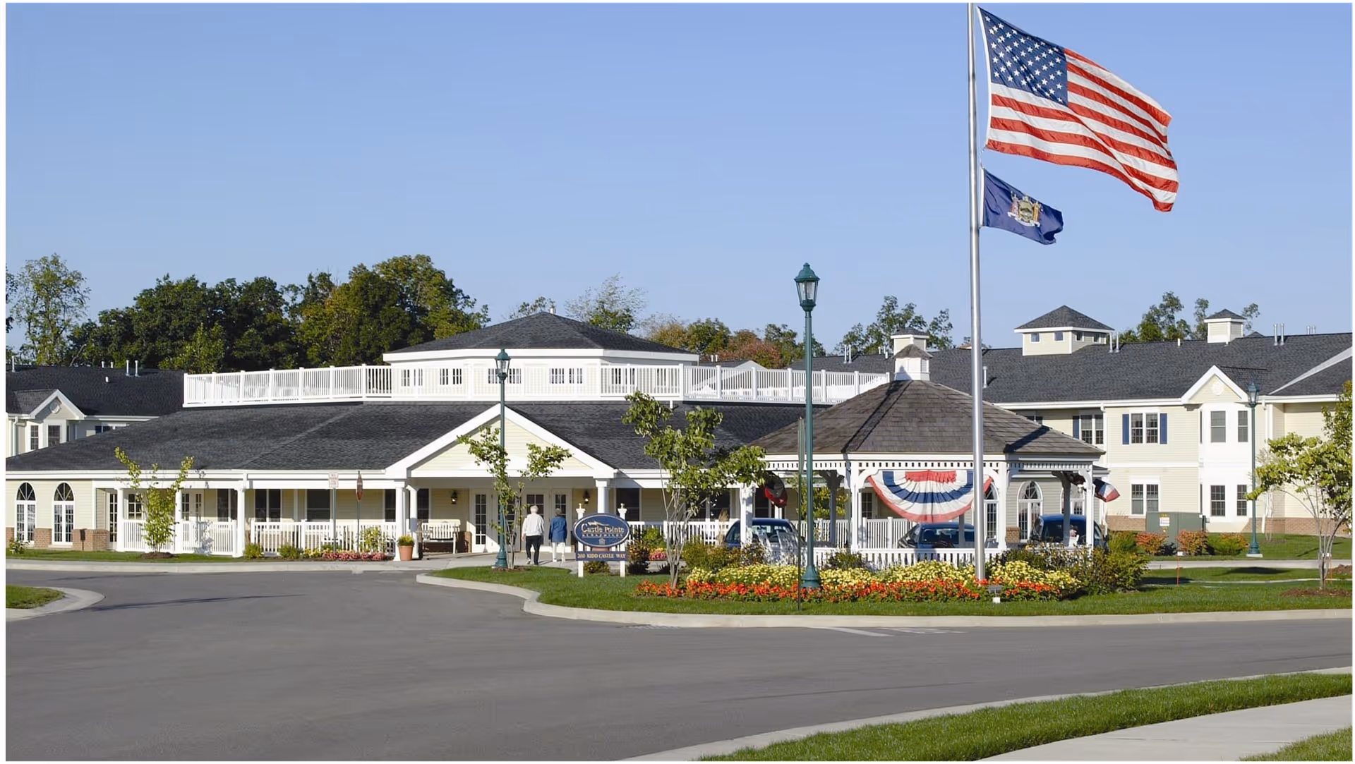 Front exterior of a senior living facility with a flagpole, gazebo, and landscaped circular driveway.