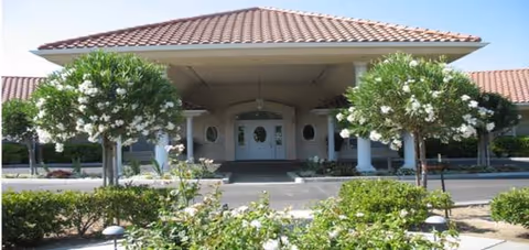Front entrance of a senior living facility with a covered porte cochere and landscaped shrubs.