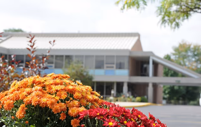 Orange and red chrysanthemums blooming in front of the entrance to a senior living facility building.
