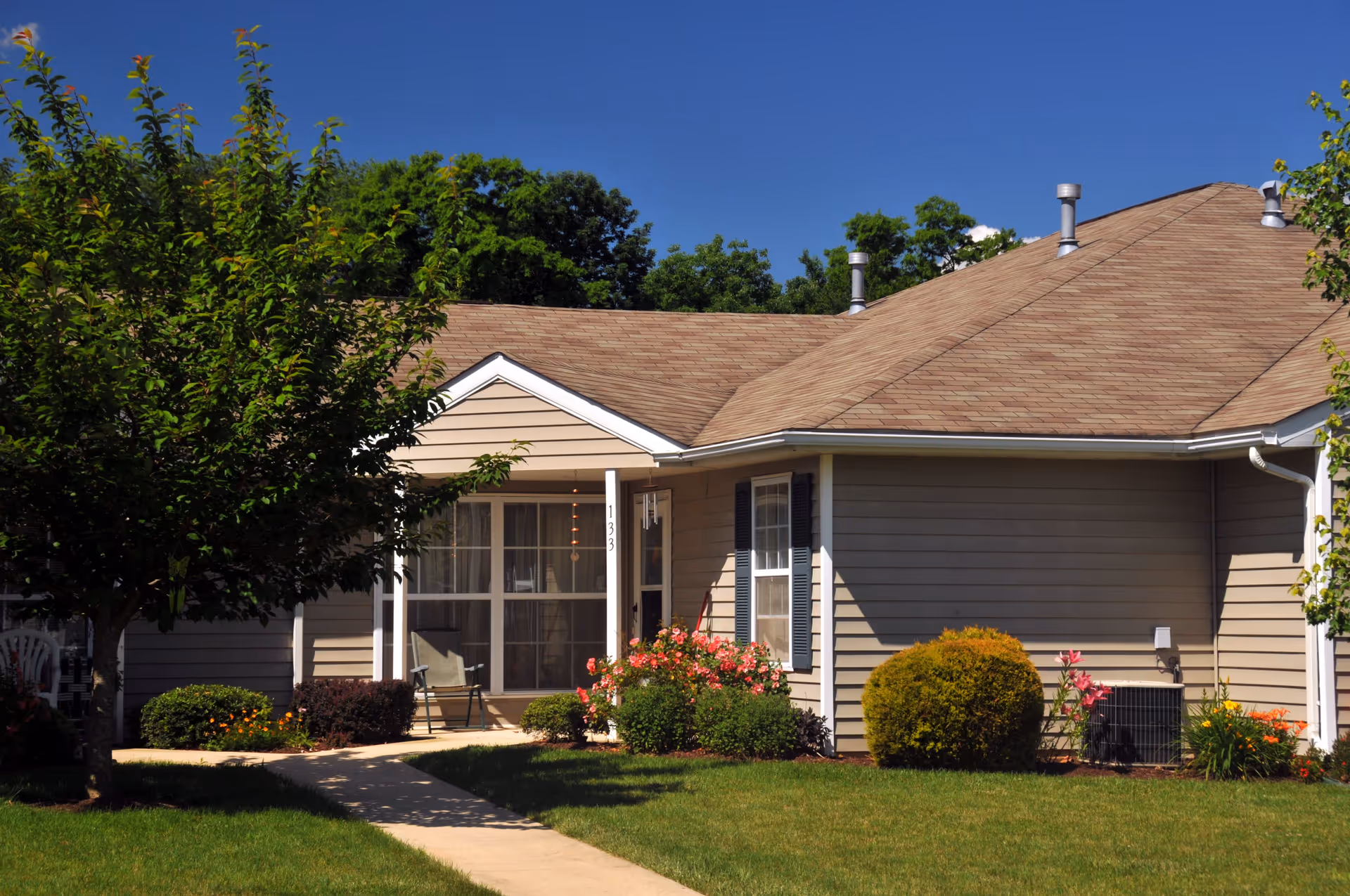 Single-story cottage-style unit with a front porch, walkway and landscaped lawn under a clear blue sky.