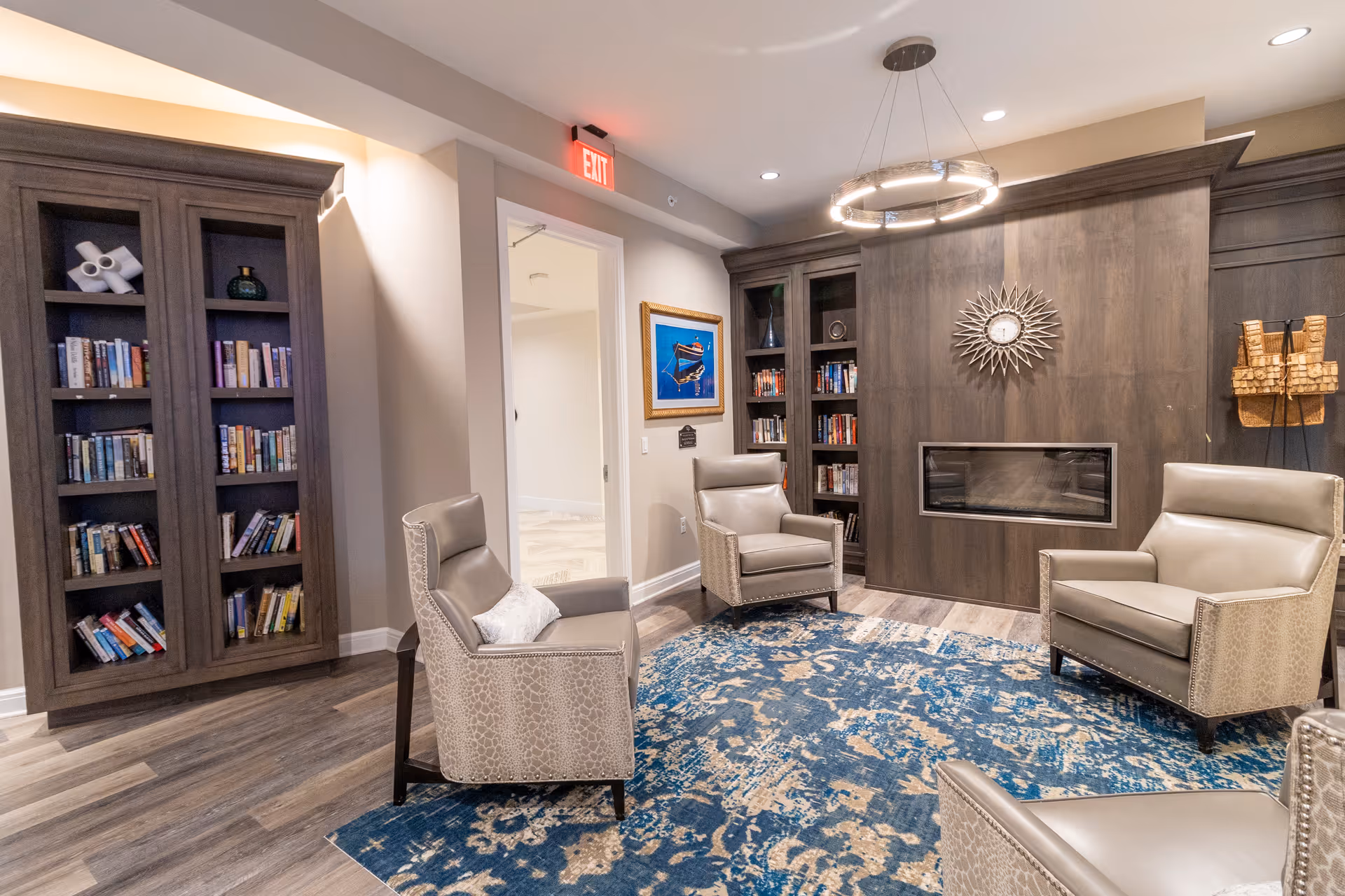 Cozy lounge with four armchairs around a blue patterned rug, built-in bookshelves, a modern fireplace, and a decorative wall clock.