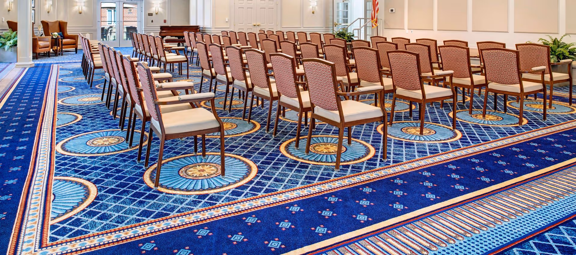 Rows of chairs arranged theater-style in a large carpeted meeting or event room with a patterned blue carpet.