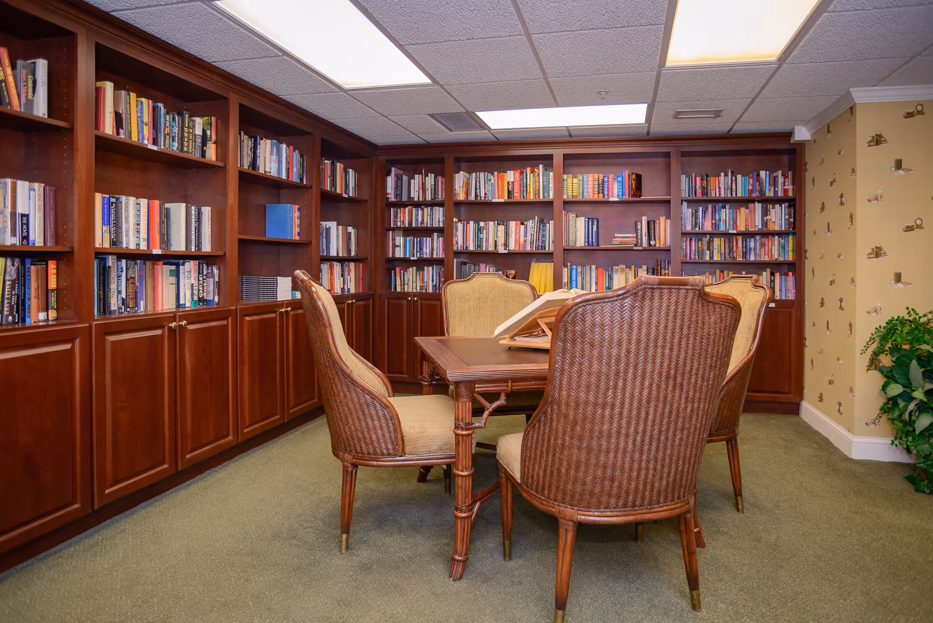 A cozy library/reading room with built-in wooden bookshelves and a table surrounded by four wicker chairs.