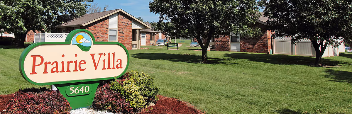 A large Prairie Villa sign on a manicured lawn with brick single-story buildings and trees in the background.