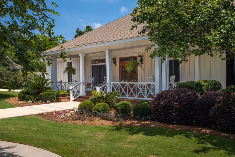 Front porch of The Brennity at Fairhope senior living with white rails, columns, and landscaping.
