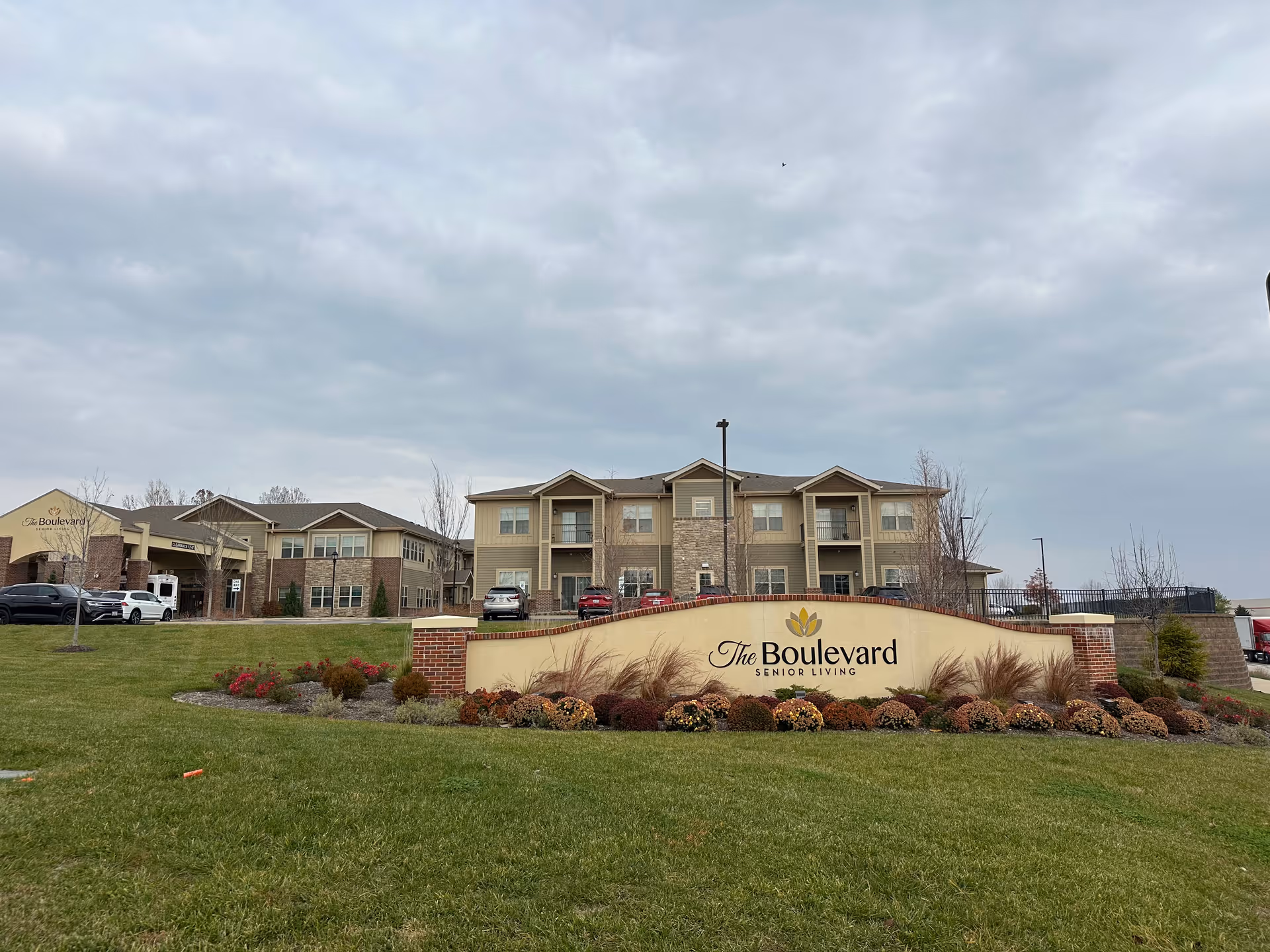 Front exterior of The Boulevard Senior Living building with its entrance sign and landscaped lawn under a cloudy sky.