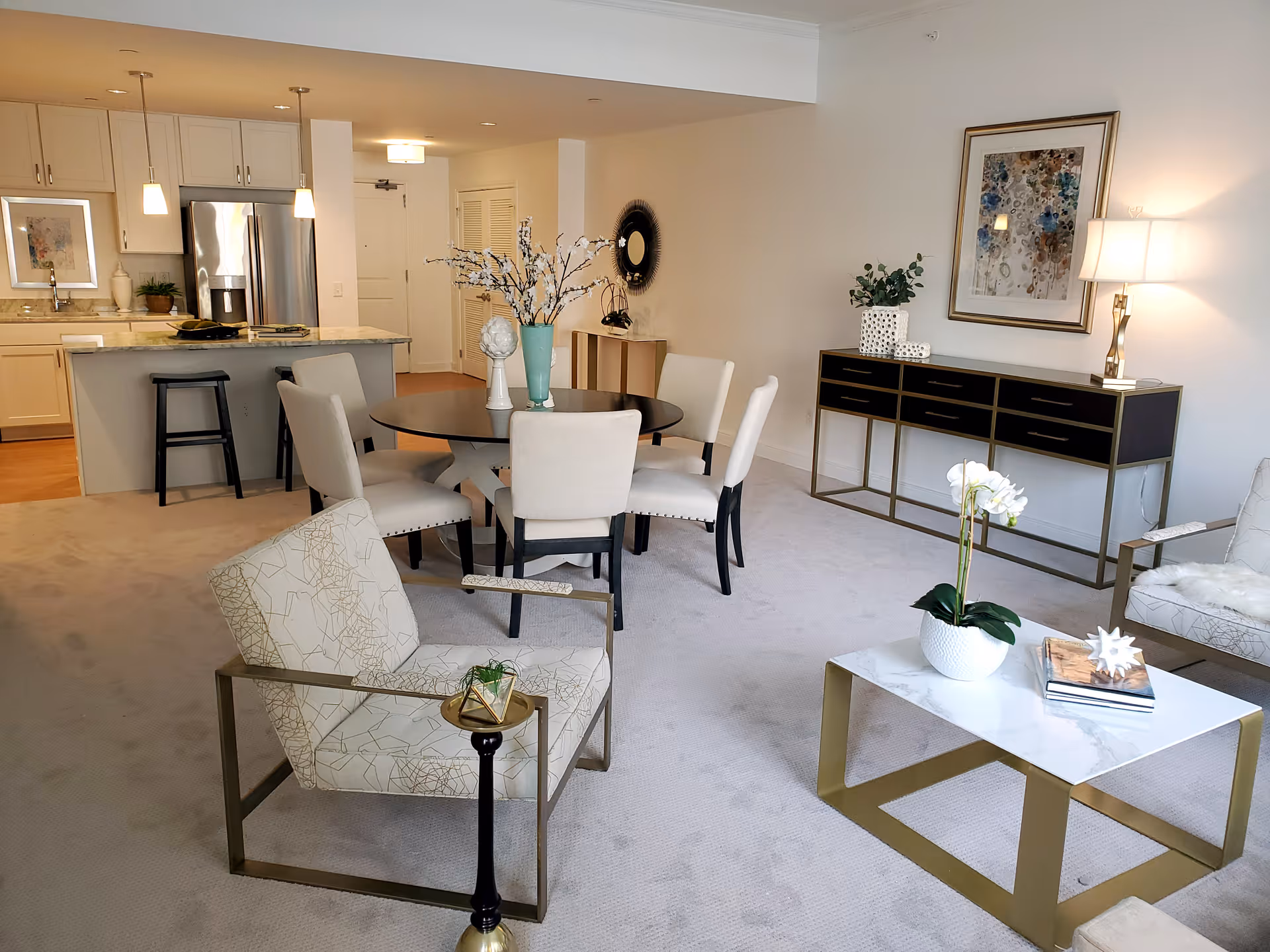 Open-plan living and dining area with seating, a round dining table, a marble-topped coffee table, and a kitchen island in the background.