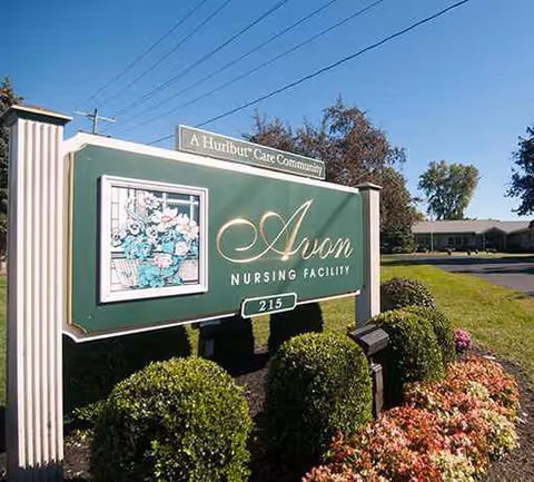 Exterior view of Avon Nursing Facility sign with shrubs and building in background.