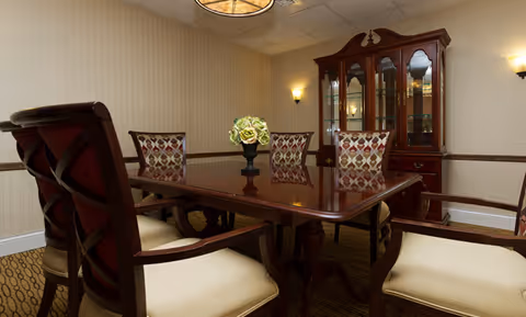 Elegant dining room with a polished wooden table, upholstered chairs, a china cabinet, and a floral centerpiece.