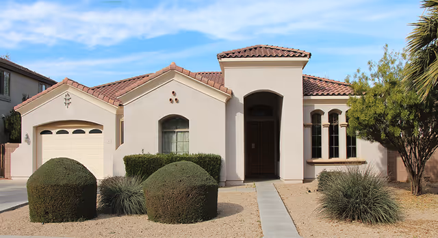 A stucco, house-style building with a front door, garage, and desert landscaping.