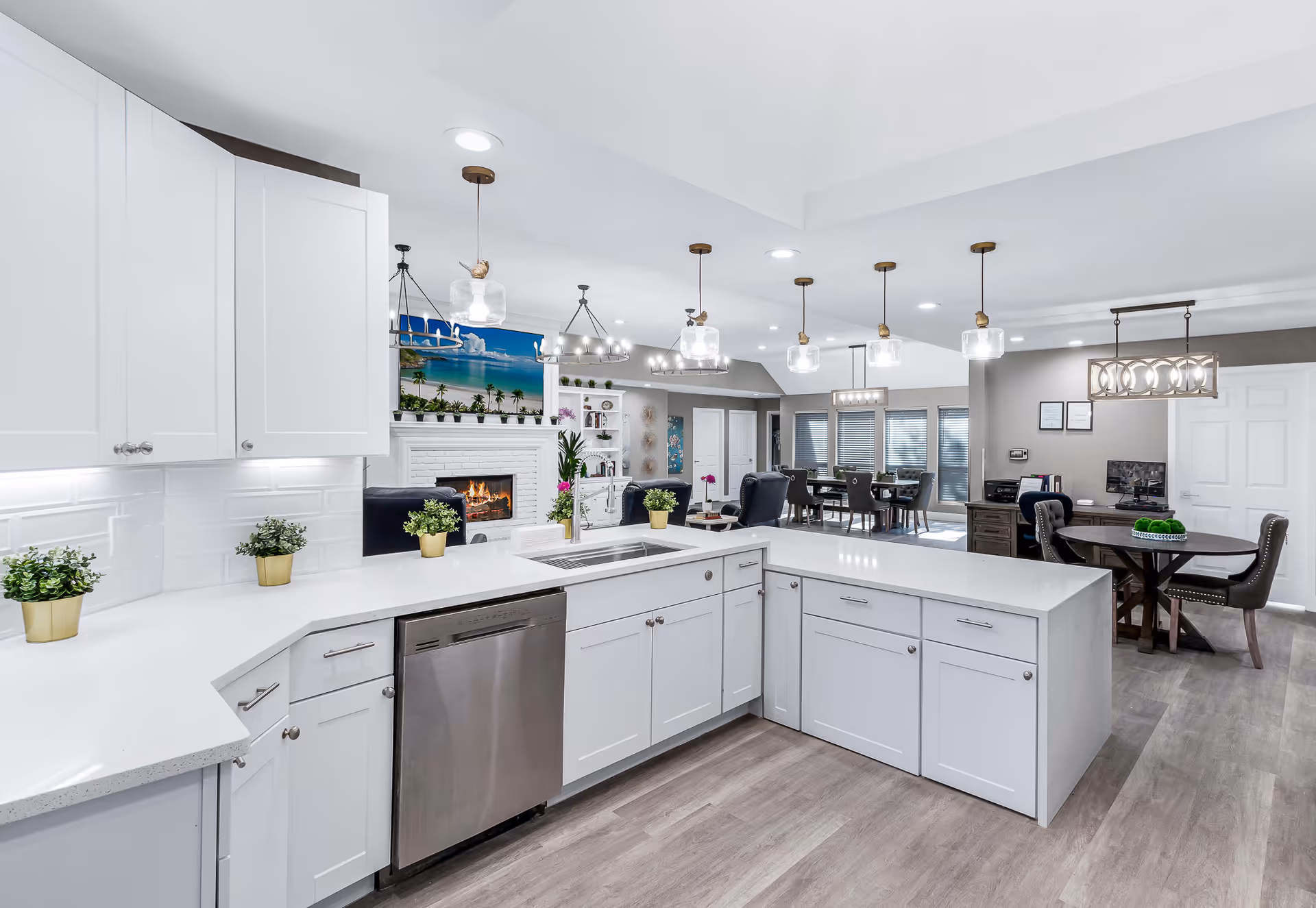 Bright modern open kitchen with white cabinets, a large island, stainless dishwasher, and pendant lights overlooking a dining and living area.