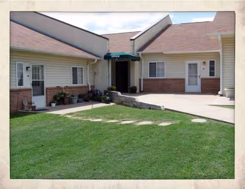 Exterior view of a senior living facility with lawn, walkway, and entrance awning.