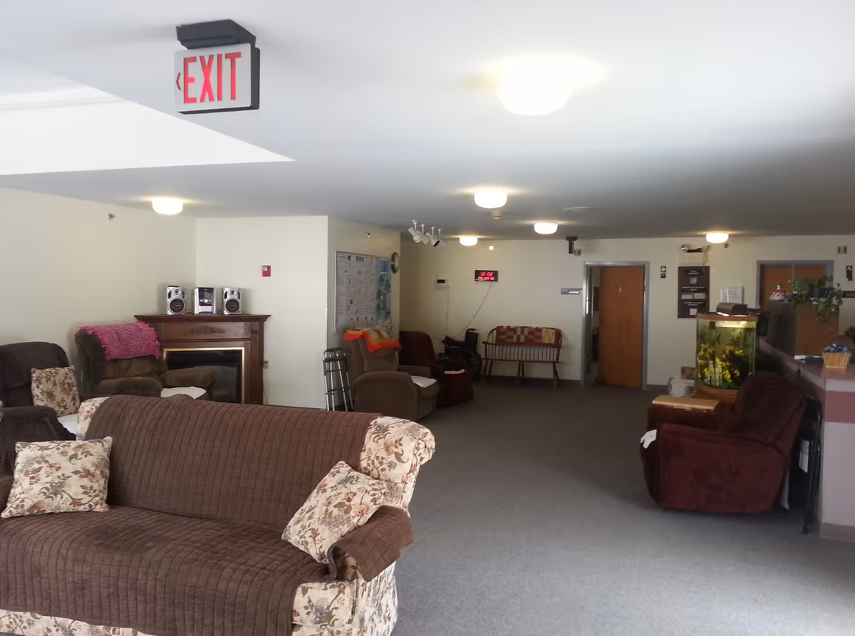 Spacious communal living room with sofas and armchairs, a fish tank, and an illuminated exit sign on the ceiling.