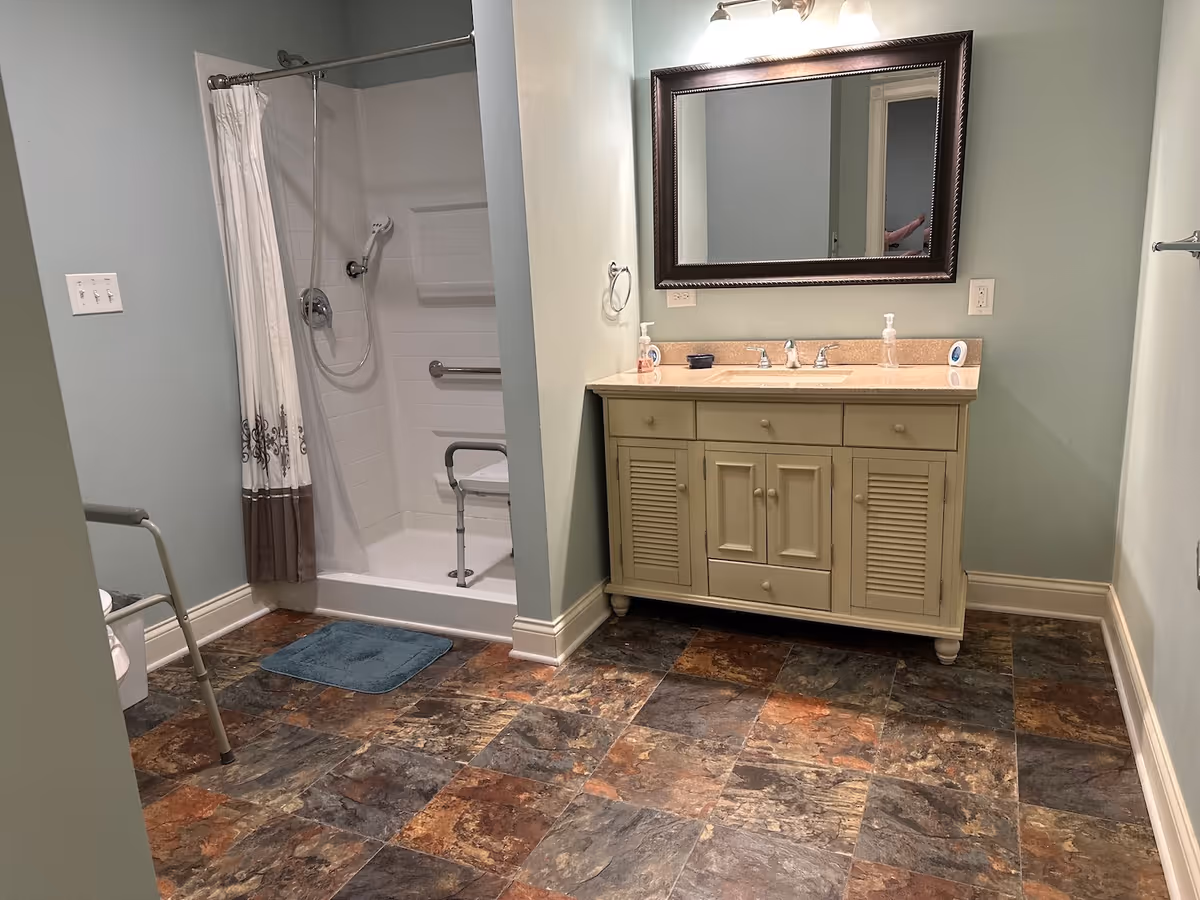 Wheelchair-accessible bathroom with a walk-in shower and shower chair, a vanity with mirror and sink, and a tiled floor.