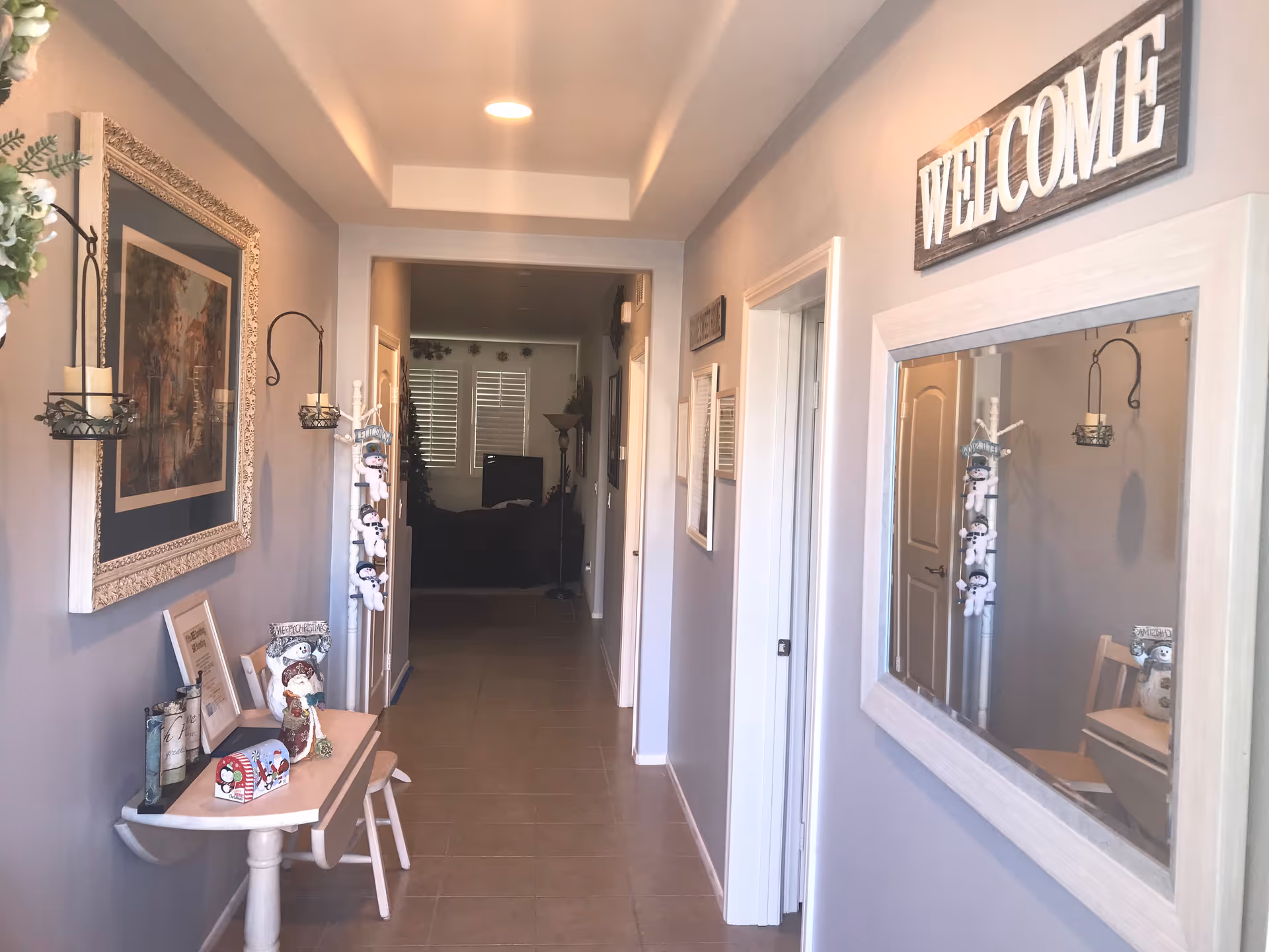 Decorated interior hallway with a console table, wall mirror and a 'WELCOME' sign leading toward a living room.