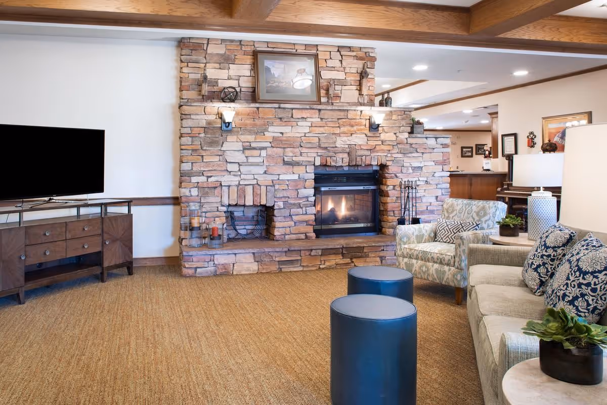 Comfortable living room featuring a stone fireplace with built-in shelving, upholstered sofa and chairs, a TV, and round ottomans.