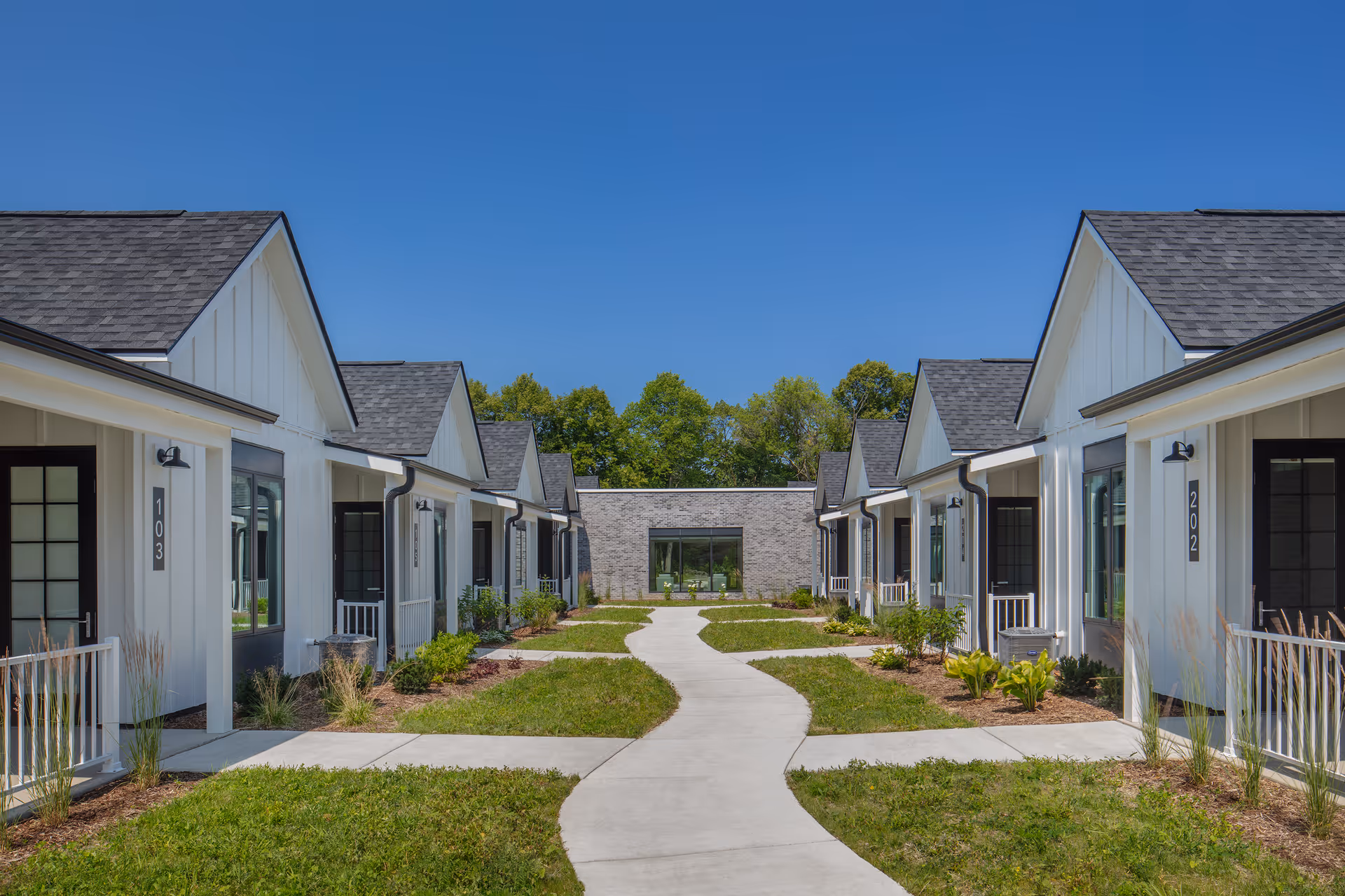 Row of single-story white cottages flanking a curving central walkway in a senior living community courtyard.