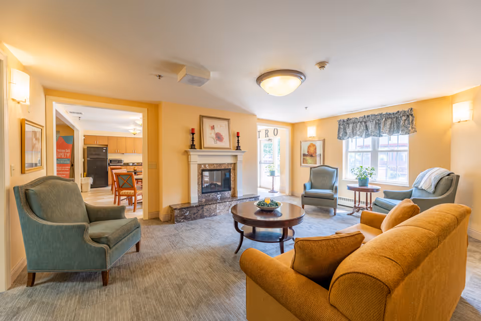 Bright furnished common living room with sofa and armchairs arranged around a coffee table and fireplace.