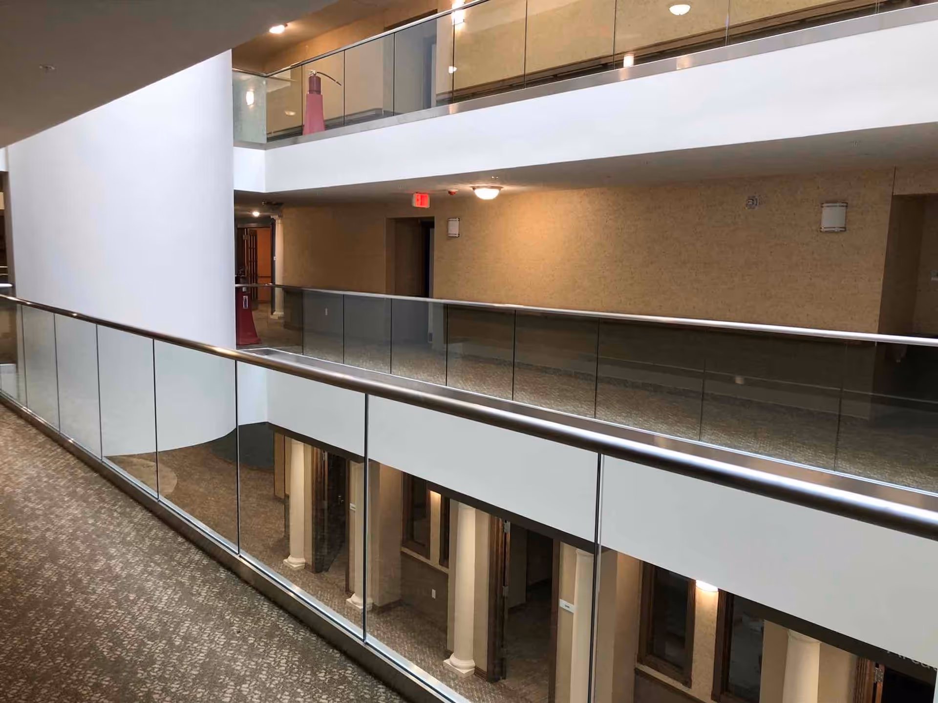 Interior multi-level atrium hallway with glass railings, carpeted floors, and corridors in a retirement community.