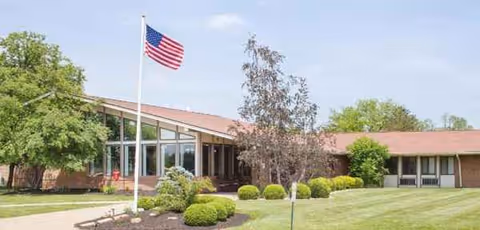 Exterior view of a brick senior living facility with flagpole and manicured lawn.