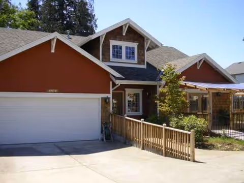 Exterior view of a residential senior living facility with a garage and wooden porch.