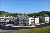 Exterior view shows a multi-building senior care campus with a curved road and green surroundings.