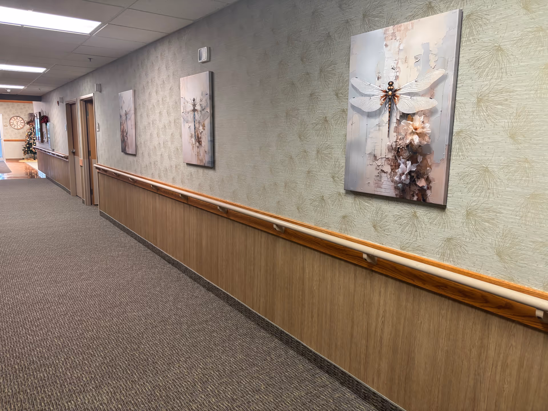 Long interior hallway with carpet, wooden handrails and framed artwork on the walls.