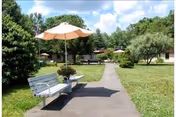 A paved walkway through a grassy courtyard with benches shaded by umbrellas and single-story buildings in the background.