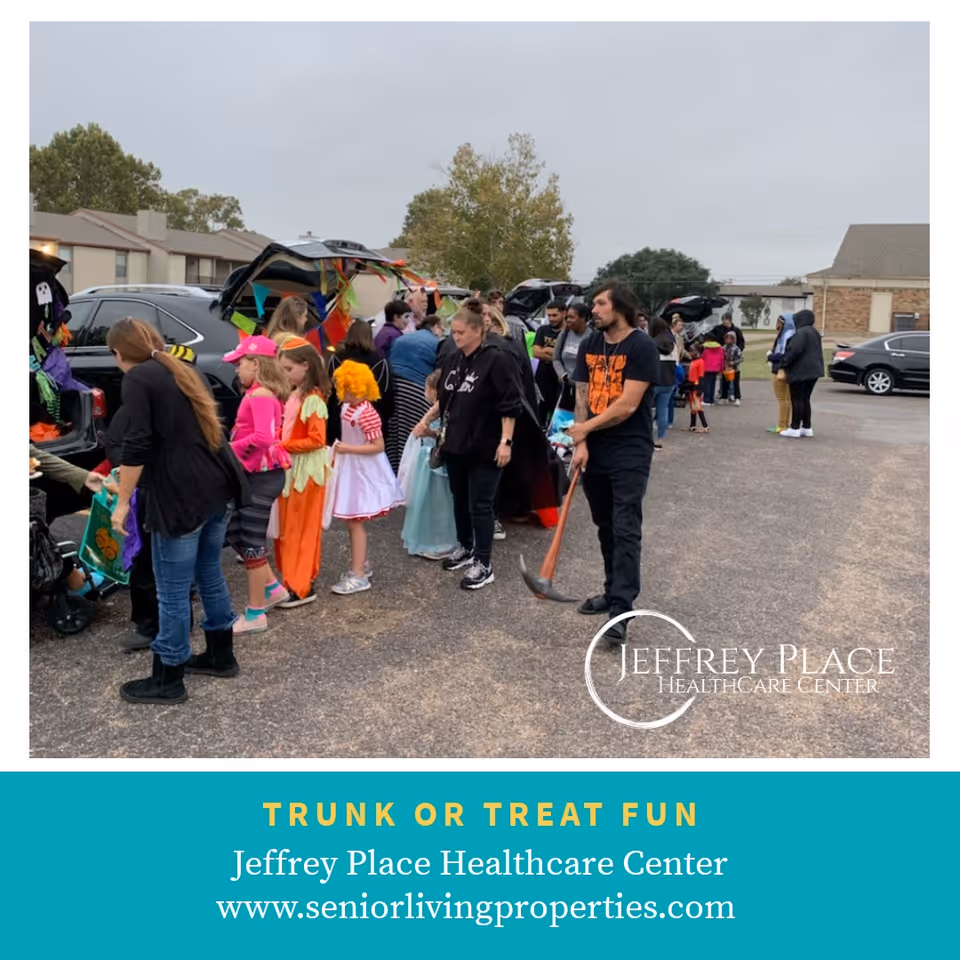 Children and adults in Halloween costumes gather around decorated car trunks in a parking lot for a trunk-or-treat event outside Jeffrey Place Healthcare Center.