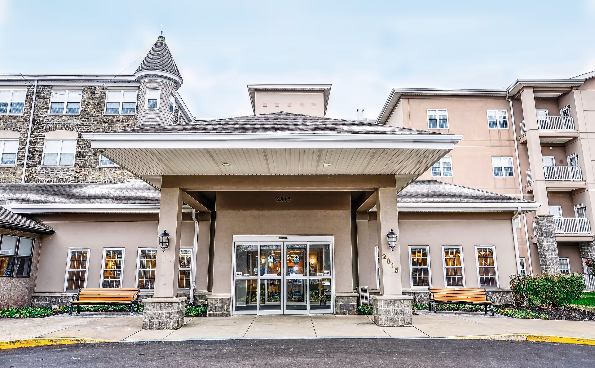 Covered main entrance with glass doors and benches at the front of a multi-story senior living building.