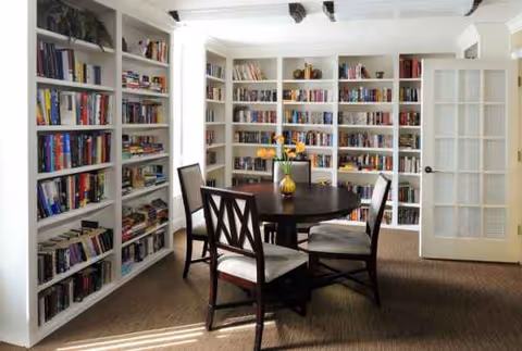 A bright library with built-in shelves, a round table, and four chairs.