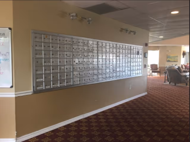 Interior hallway/lobby showing a long wall of metal mailboxes above a patterned carpet leading to a seating area.