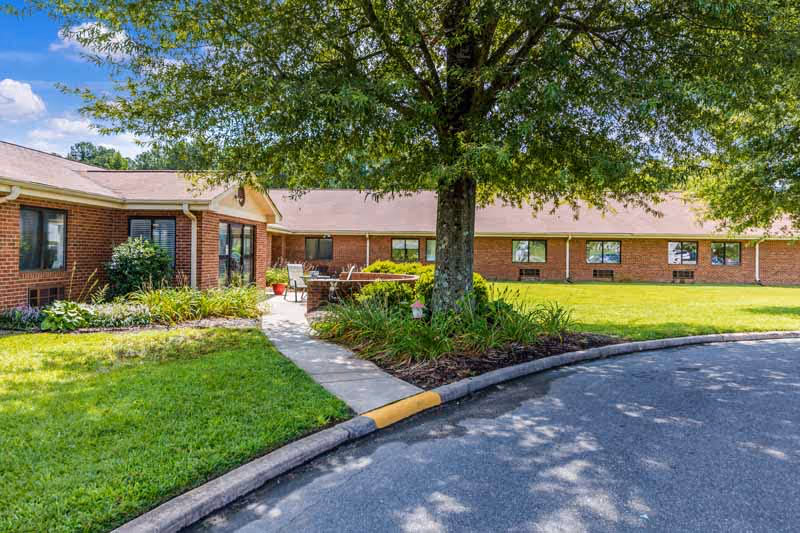 Single-story brick rehabilitation facility exterior with a shaded courtyard, walkway, and circular driveway.