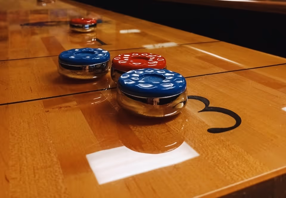 Close-up view of a shuffleboard table with blue and red pucks positioned on the wooden playing surface marked with the number 3.