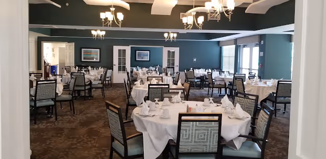 Spacious dining room with multiple round tables set with white tablecloths and place settings beneath chandeliers.