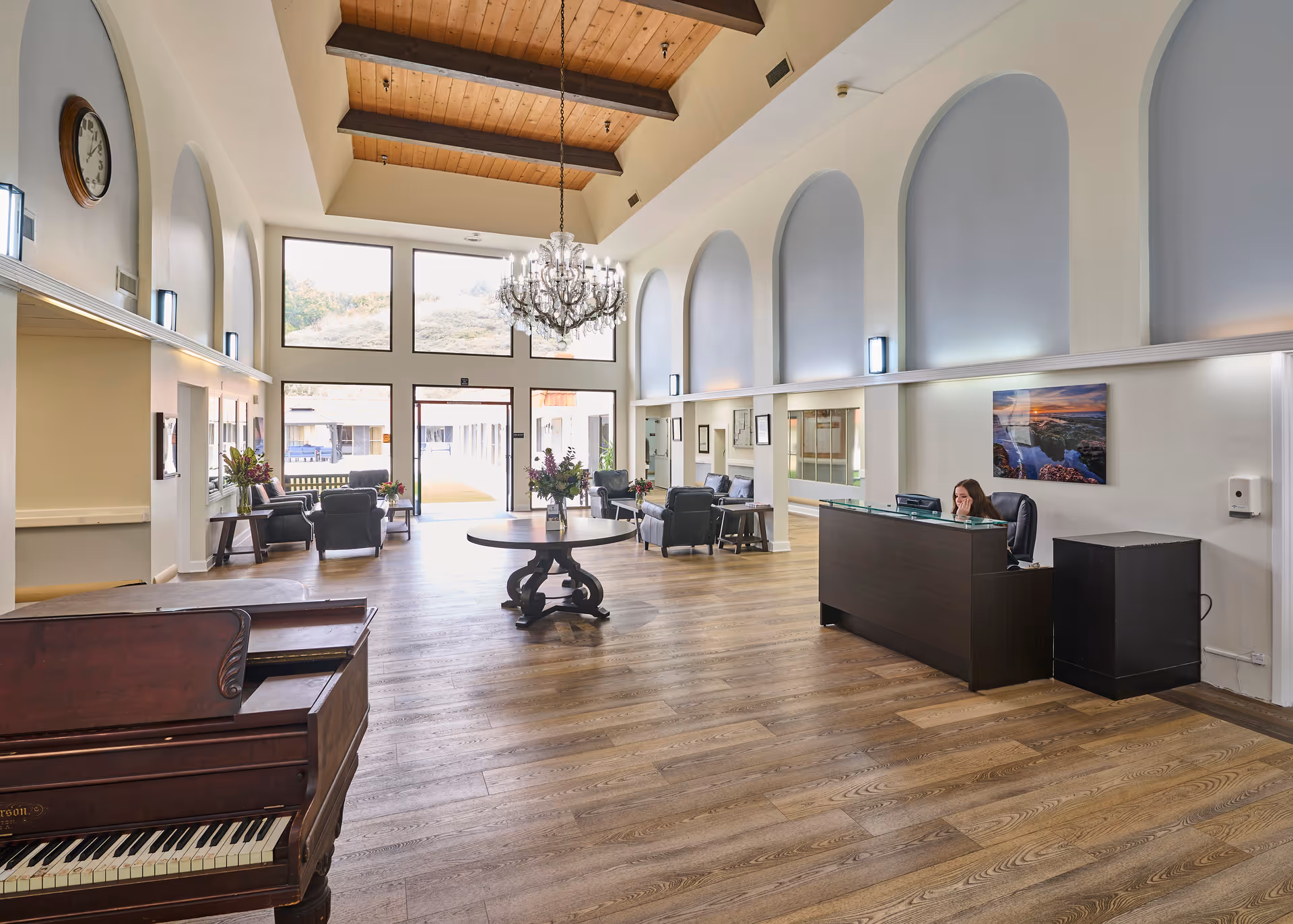 Spacious high-ceilinged nursing home lobby with a reception desk, seating areas, chandelier and a piano.